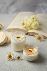 Fototapeta na wymiar Burning scented candles and chamomile flowers on light gray textured table