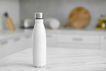 Stylish thermo bottle on white table in kitchen. Space for text