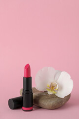 Obraz na płótnie Canvas Beautiful lipstick and orchid flower on stone against pink background