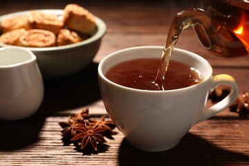 Pouring aromatic anise tea into cup on wooden table