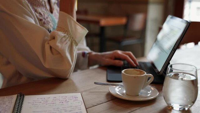 POV overhead closeup view of mature elderly woman hands typing on laptop tablet computer wearing ethnic clothes in a cafe coffee shop.