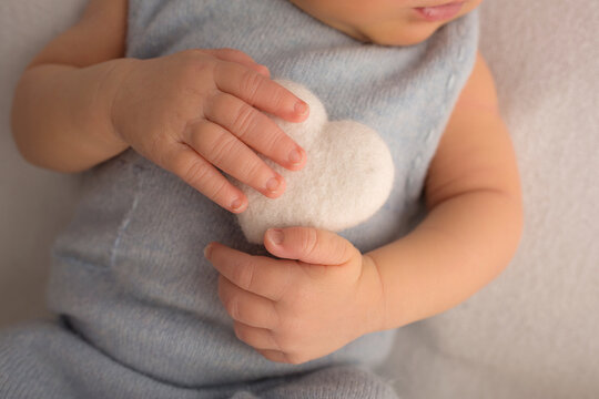 Child's hand, fingers close up. Newborn holding a soft heart in his hands. 