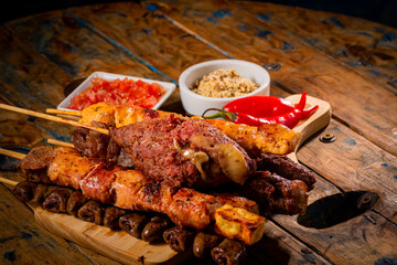 Espetinhos de churrasco em tábua de madeira com acompanhamentos, arroz, vinagrete, farofa e maionese