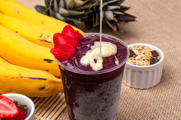 Acai in plastic cup with strawberry, banana, granola and condensed milk. Brazilian popular food.