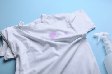 White shirt with purple stains and detergent on light blue background, above view