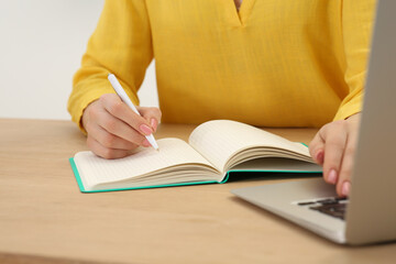 Woman writing in notebook at wooden table indoors, closeup