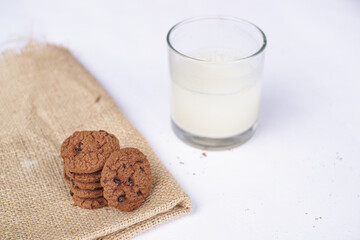 A glass of fresh milk with some cookies on a brown cloth mat is isolated on a white background.