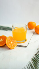 A glass of fresh orange juice with half-cut and sliced orange fruits and a green leaf isolated on a white background.