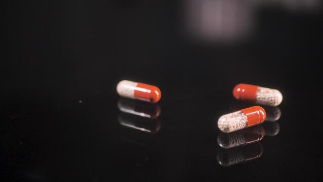 Pills falling down on a black glass surface,  mirror surface with a reflection on black background. Spinning and rotating.