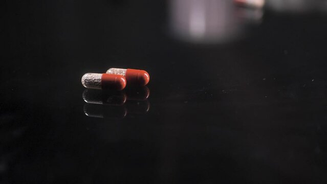 Pills rolling on a black glass surface,  mirror surface with a reflection on black background. Spinning and rotating. Solwmotion.