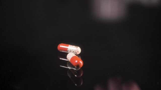 Pills falling down and rolling on a black glass surface,  mirror surface with a reflection on black background. Spinning and rotating. Solwmotion.