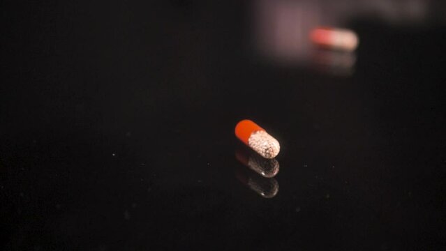 Pills falling down on a black glass surface,  mirror surface with a reflection on black background. Spinning and rotating. Solwmotion. Scene B.