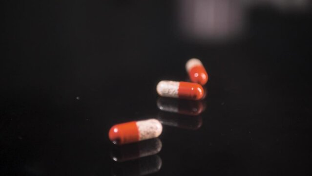 Pills falling down on a black glass surface,  mirror surface with a reflection on black background. Spinning and rotating. Scene B.