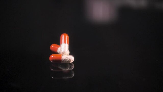 Pills falling down on a black glass surface, mirror surface with a reflection on black background. Spinning and rotating. Solwmotion.