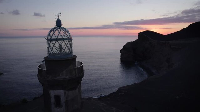 Aerial pullback closely past Capelinhos Lighthouse at sunset, Faial Island