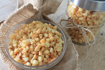 Indonesian snack in the form of small fried cassava slices called balok in a glass bowl lined with burlap and a glass jar on a wooden table

