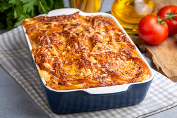 Pasta casserole bechamel sauce topped with melted mozzarella cheese and served in a white baking dish on a table (Turkish name; firinda makarna or firin makarna)