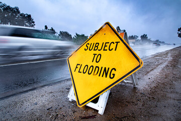 Road Sign stating Subject to Flooding with rainy highway in the bacground