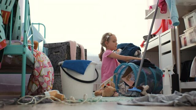 Little girl carefully folding her clothes while cleaning her messy room. Concept of household chores and housework