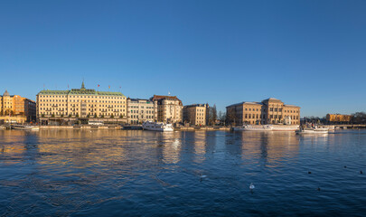 Fototapeta premium The bay Strömmen museums, moored boats and hotels on a pier a low winter solstice a sunny and snowy day in Stockholm
