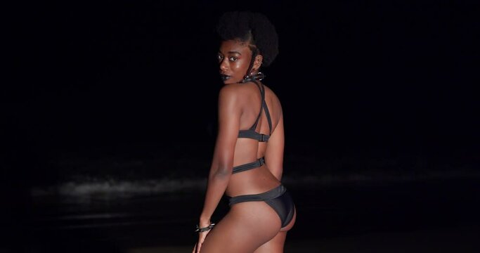 Young woman enjoys the sea breeze in a black bikini at night on the beach in the Caribbean