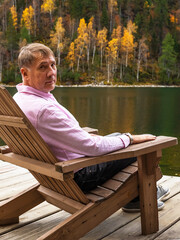 Man resting in Comfortable wooden sun lounger Adirondack, Westport against of colorful mountains with emerald lake