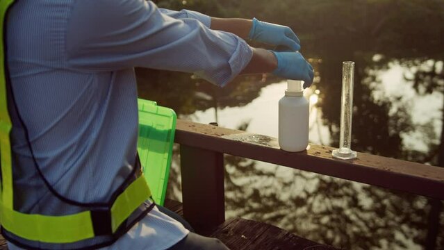 Environmentalist collectings sample water from the pond to measuring cylinder then looks closely to examine water quality which presents environmental or pollution and contamination concepts.