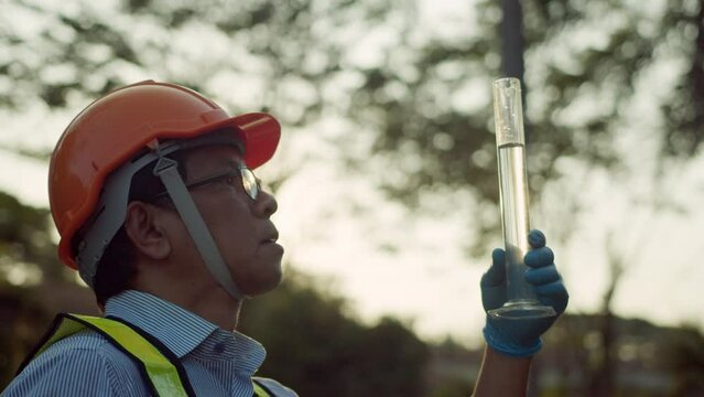 Environmentalist collectings sample water from the pond to measuring cylinder then looks closely to examine water quality which presents environmental or pollution and contamination concepts.