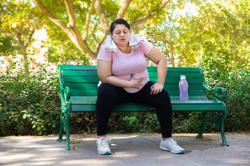 Overweight tired exhausted indian woman sitting outdoors in park after jogging workout. Fat lady...