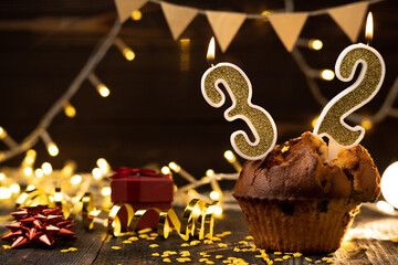 Number 32 birthday celebration candle in cupcake against lights and wooden background