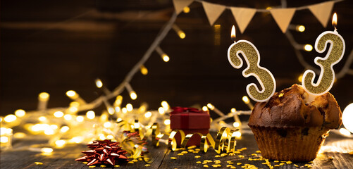 Number 33 birthday celebration candle in cupcake against lights and wooden background.