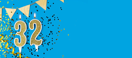 Number 32 gold celebration candle on blue background.