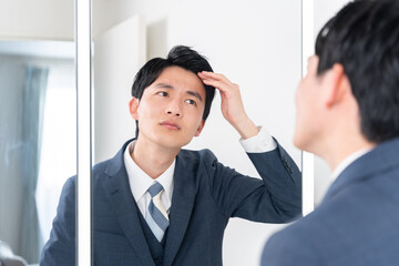 洗面所で鏡を見て髪の生え際をチェックする若いビジネスマン