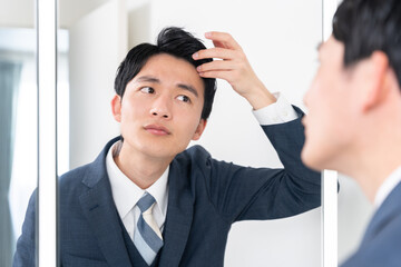 洗面所で鏡を見て髪の生え際をチェックする若いビジネスマン