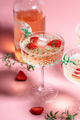drink cocktail with ice in a glass on pink background. refreshing fruit cocktail or punch with wine champagne, strawberries, ice and rosemary