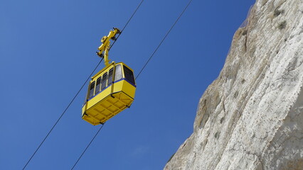 Yellow funicular car against the background of the sky and white rock in the village of Rosh ha nikra in the north of Israel.