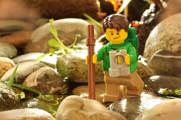 Naklejka premium Lego minifigure of happy boy with binocular on stone in nature by day light. Editorial illustrative image of travel or vacation on nature.