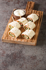 Norwegian roll of smoked salmon, cream cheese and herbs wrapped in flat bread close-up on a wooden board on the table. Vertical