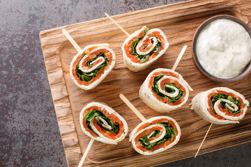 Appetizer of wrapped smoked salmon fillet, cream cheese and herbs in a flat bread close-up on a wooden board on the table. horizontal top view from above