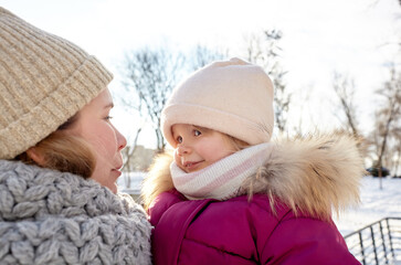 Mother and daughter are walking in the winter city park on Christmas and New Year holidays. Parent and little child having fun outdoors