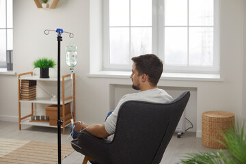 Rare view of male patient receiving intravenous treatment. Young man sitting in armchair during...