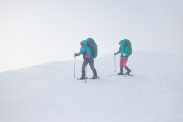 two girls with a backpack and snowshoes walk in the snow during a snow storm.