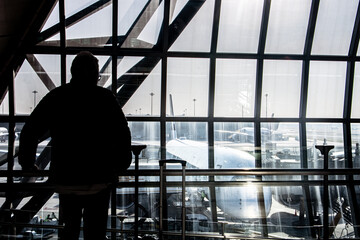 Fototapeta na wymiar Dark silhouette of passengers in front of windows in airport hall with view of plane at departure gate