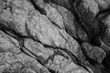 Abstract texture of the stone of the sea shore with cracks in black and white toning.