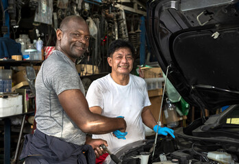 Black car mechanic man checking hand with Asian mechanic assistance in auto repair shop during fixing vehicle, Car Mechanic Concept