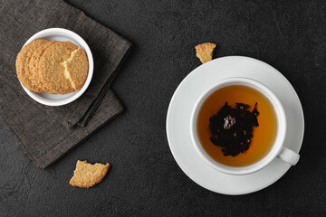 Cup of tea with cookies on black background.