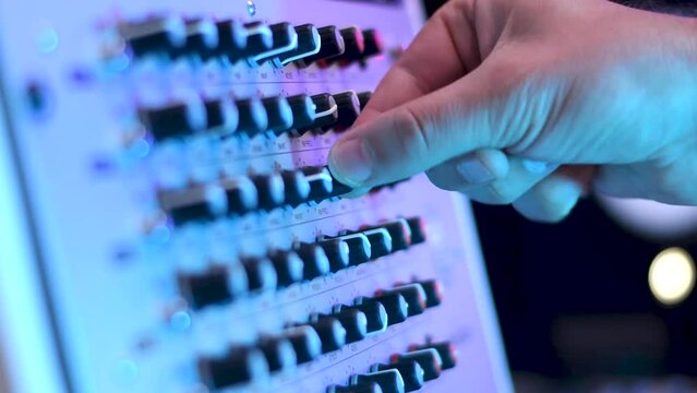 Man turning adjusting knob parameter on analogue drum synthesiser drum machine in a dark studio room with hand