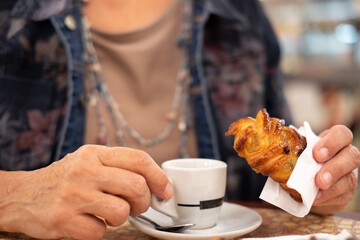 Blurred senior woman sitting at a cafe table while enjoying a break with an espresso coffe cup and...