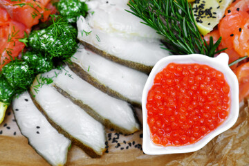 Fillet mix of red and white fish cut into slices with oil, red caviar and lemon, restaurant serving