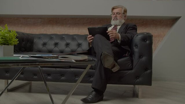Successful handsome bearded senior male CEO networking online on business project using digital tablet, analyzing current trends of market and financial data while working at office.